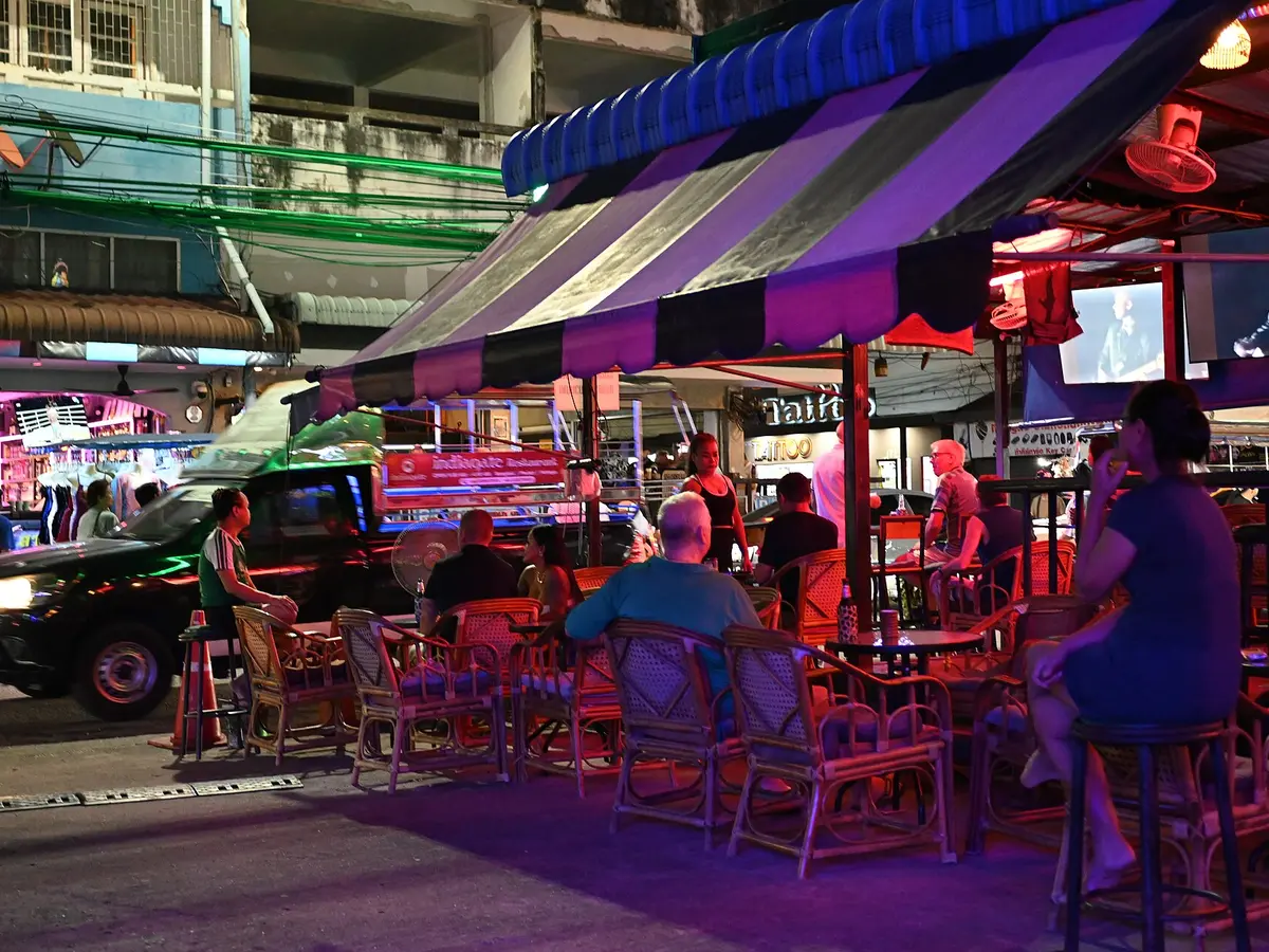 DFC 1698 Nighttime street-side bar with patrons seated under a striped awning as colorful neon lights wash the scene.jpg｜PattayaPatrol